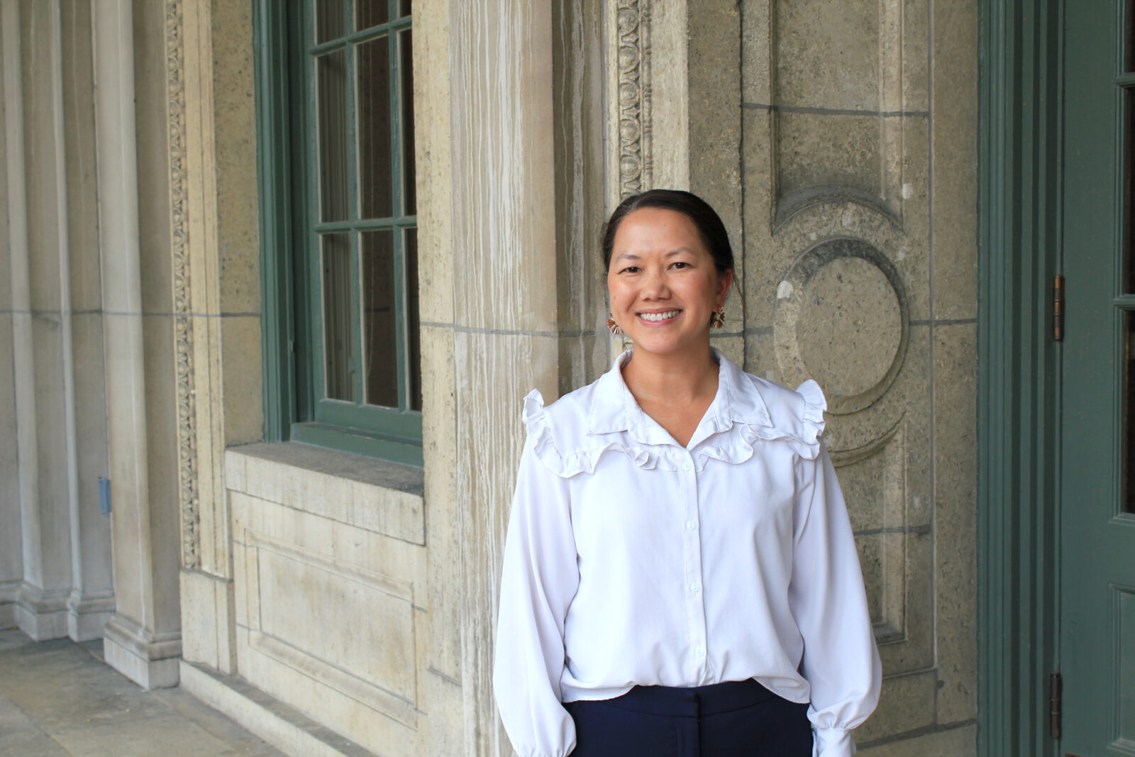 Bio picture of CeO Alumni, Pa Her, wearing a white colored button-up dress shirt in front of a brick structure.